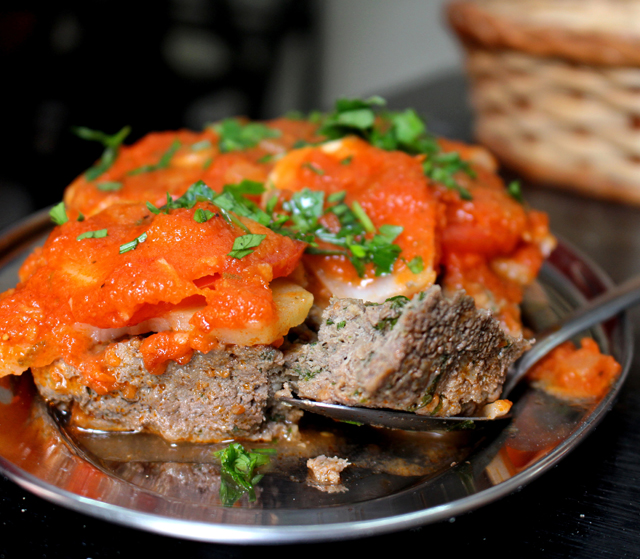 Kafta Bi Siniye: na bandeja, coberta por molho de tomate, batata, cebola e tomate