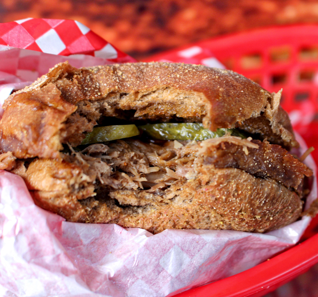 Sanduíche de suculento pulled pork - carne de porco defumada, assada longamente e desfiada - com picles de pepino artesanal no macio pão australiano